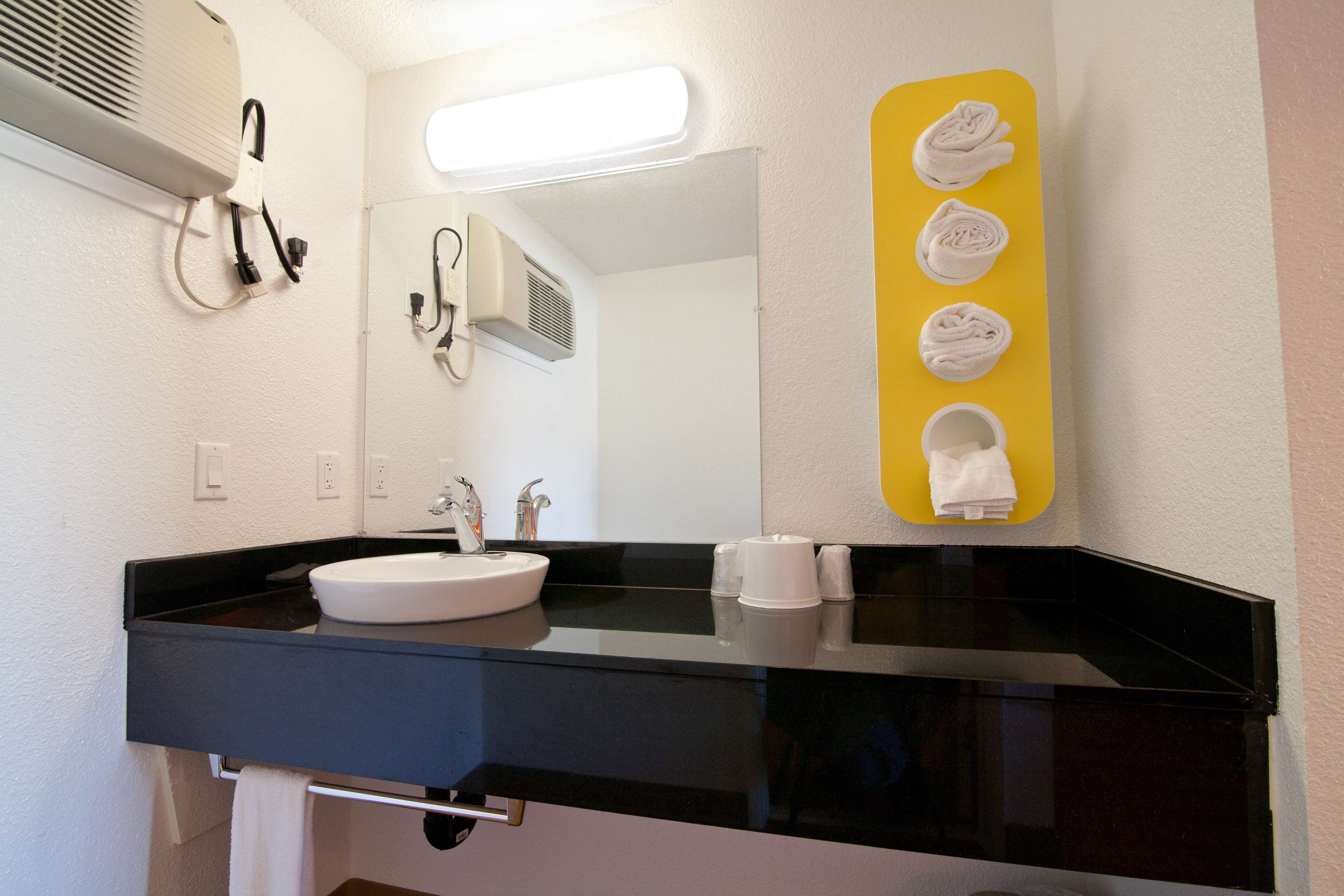 A modern bathroom with a black countertop, white sink, and a mirror. There are towels hanging on a yellow rack and a white towel on the counter.