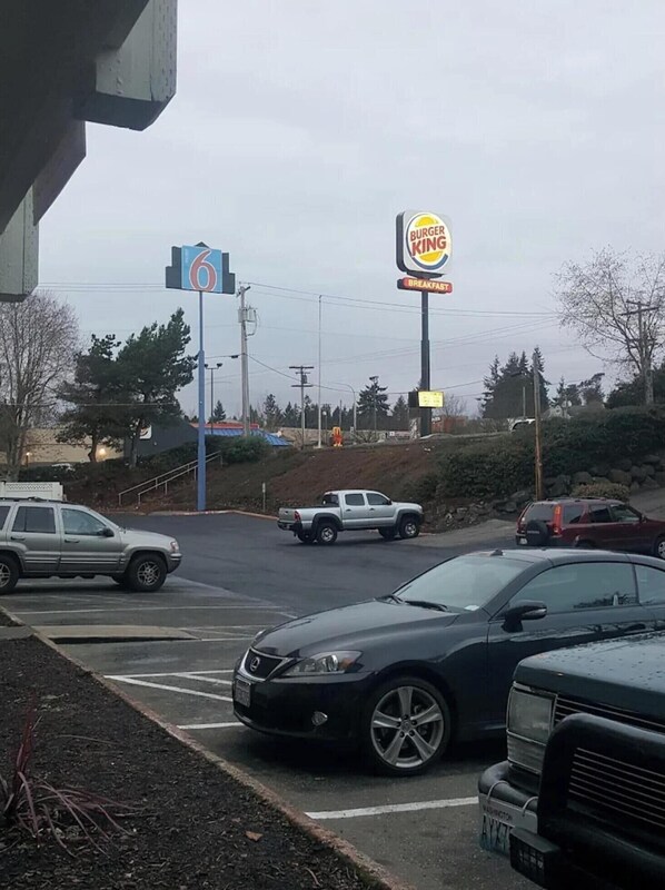 Een Burger King bord en een blauw bord met het nummer 6 aan een straat met geparkeerde auto's.