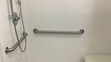 A shower area with a grab bar, a handheld showerhead, and a wall-mounted faucet.