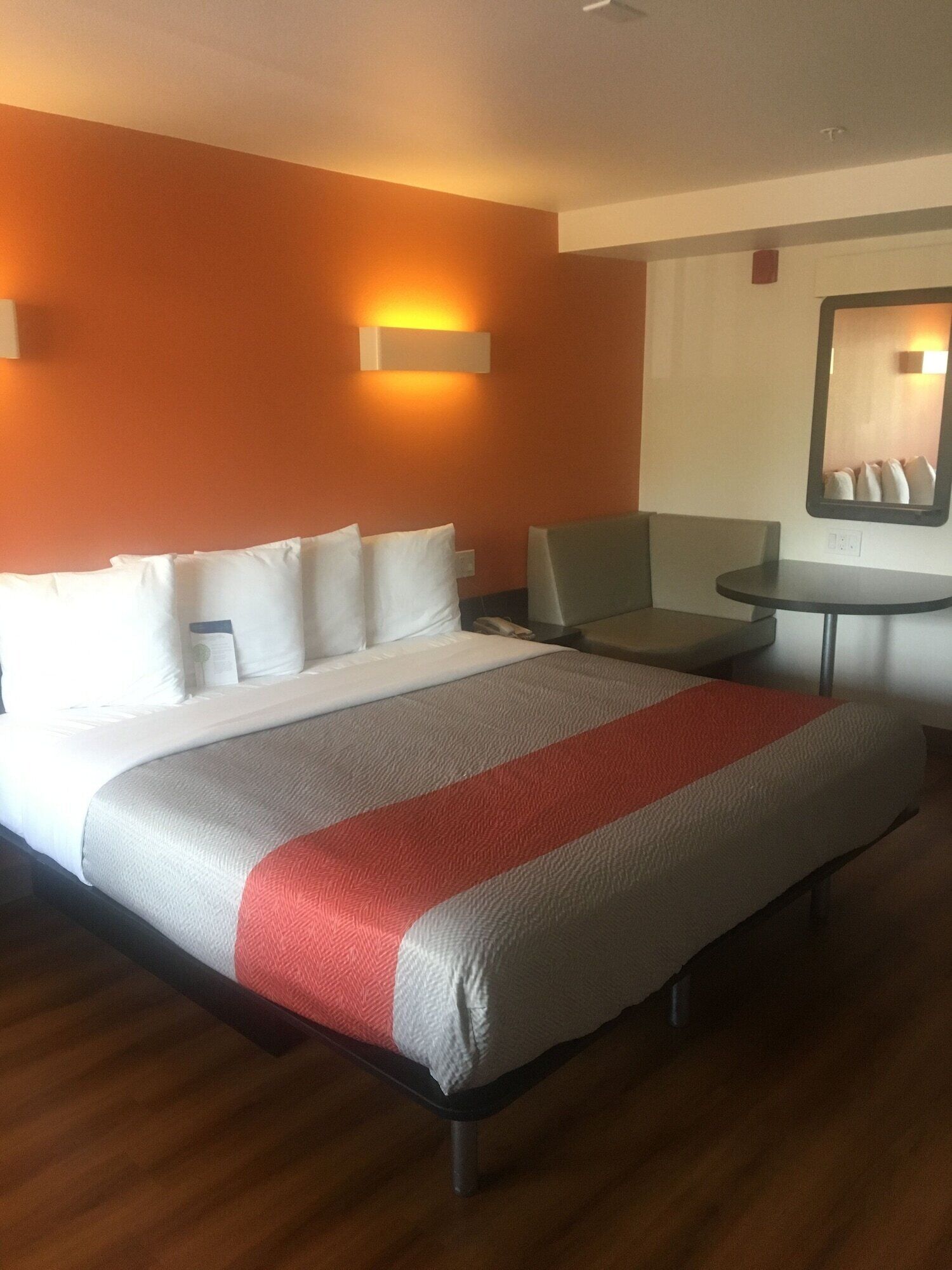 A hotel room with a large bed, a small table, a chair, and a mirror on the wall.