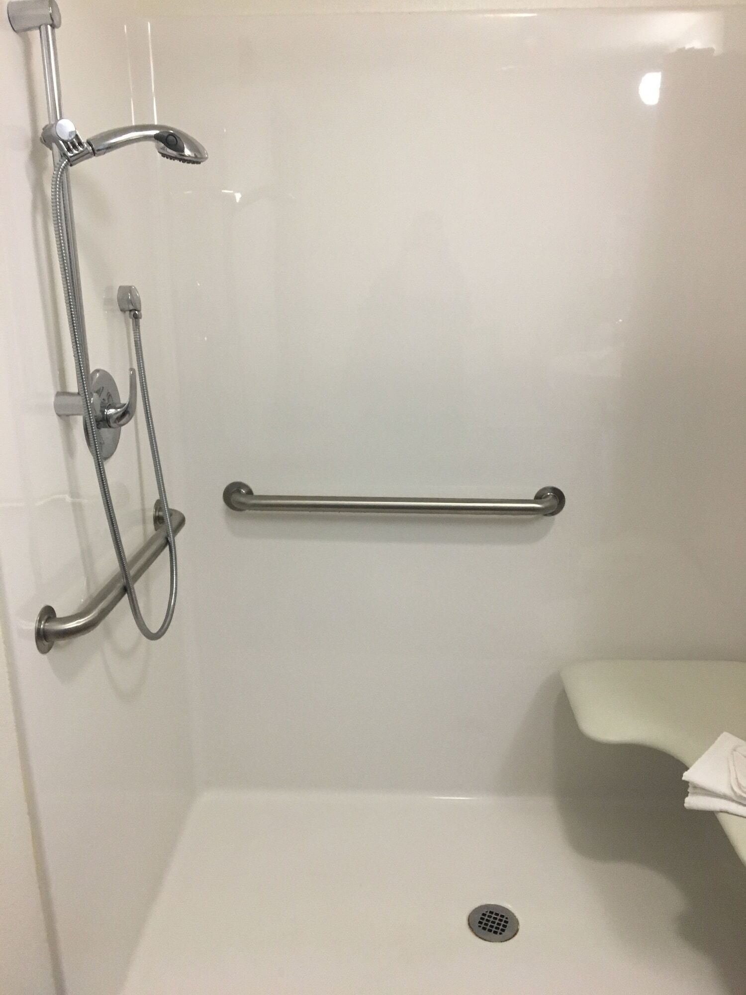 A shower area with a grab bar, a handheld showerhead, and a wall-mounted faucet.