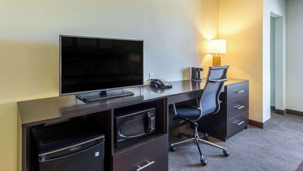 A hotel room with a flat-screen TV, a desk with a lamp, a microwave, and a chair.