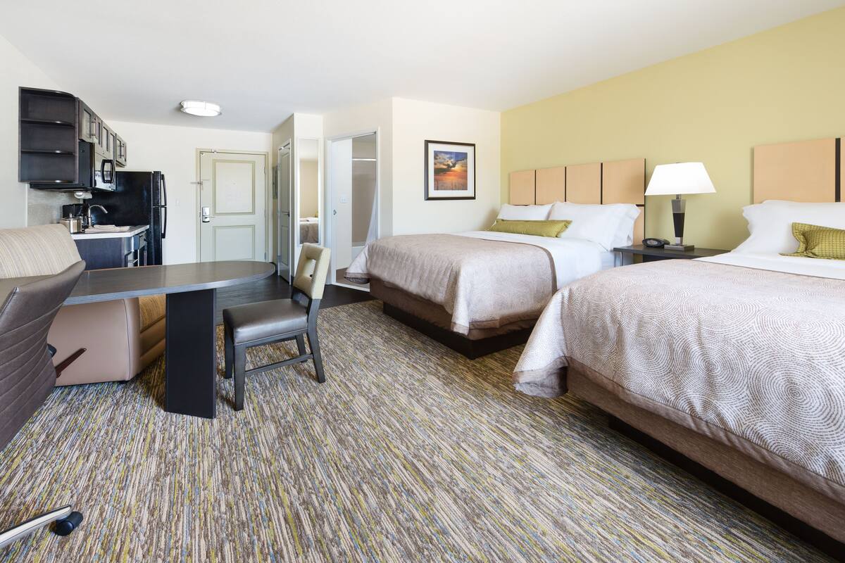 Une chambre d’hôtel avec deux lits, un bureau, une chaise, une kitchenette et une salle de bain.