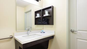 A bathroom with a white sink, a mirror, a towel rack, and a shelf with toiletries.