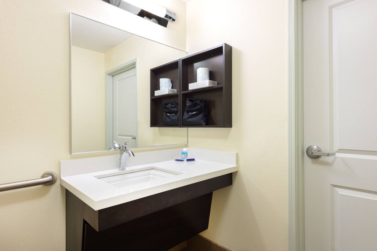 Une salle de bain avec un lavabo blanc, un miroir et une étagère contenant des articles de toilette.