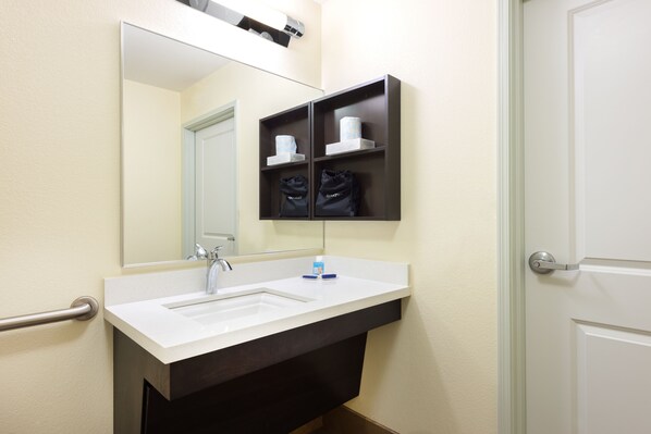 A bathroom with a white sink, a mirror, and a shelf with toiletries.