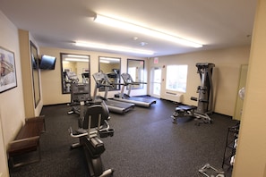 A gym with treadmills, weight machines, and a mirrored wall.