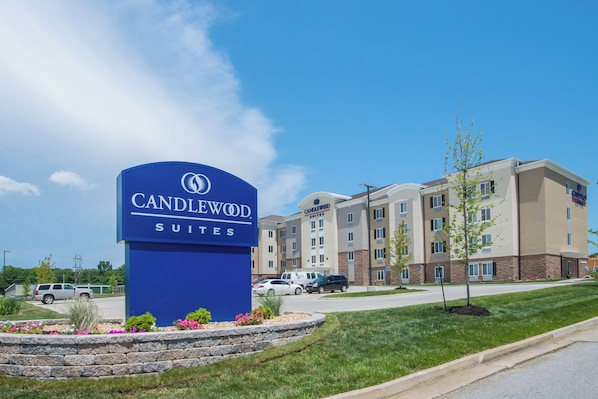 Un letrero de hotel con 'CANDLEWOOD SUITES' y un edificio de varios pisos con fachada de piedra.