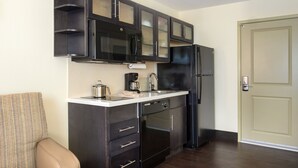 Cocina compacta con armarios oscuros, microondas, cafetera y refrigerador.