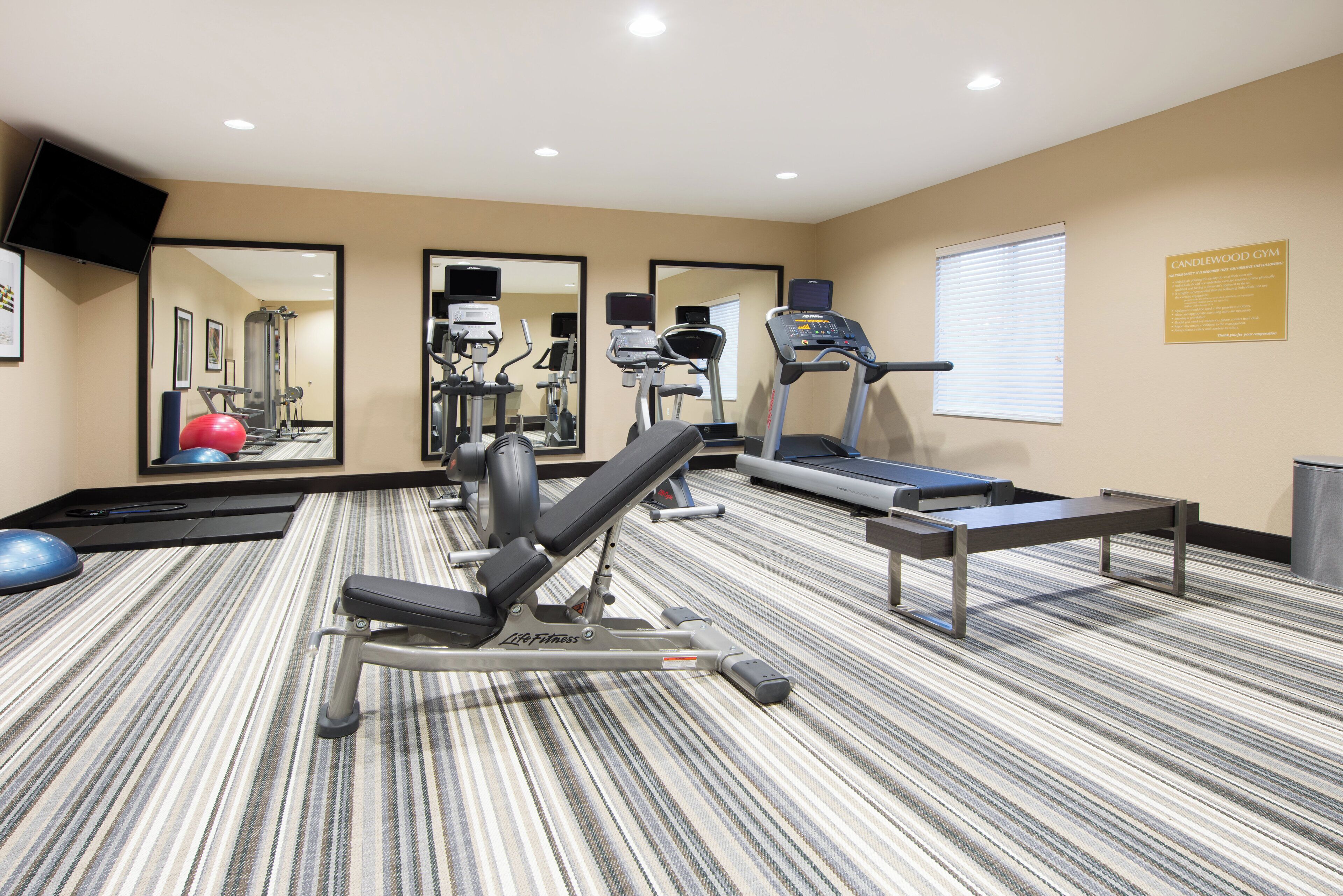 Un gimnasio con equipo de ejercicio, un espejo grande y una ventana con persianas.