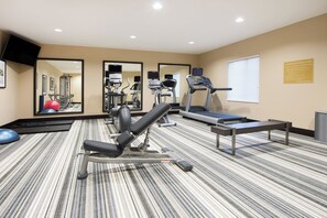 Un gimnasio con equipo de ejercicio, un espejo grande y una ventana con persianas.