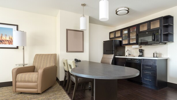 A modern hotel room with a dining area, a sofa, a flat-screen TV, a microwave, and a coffee maker.