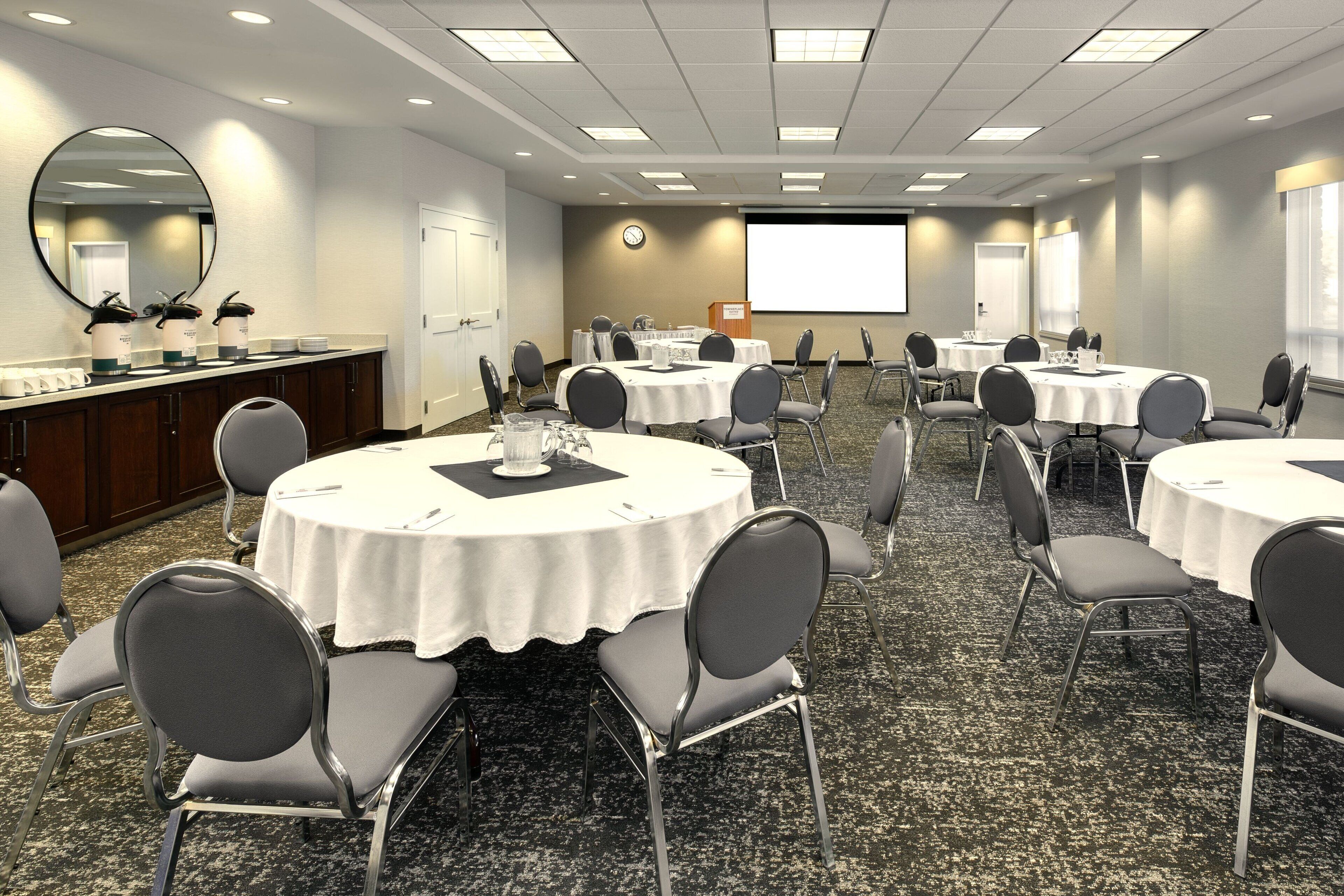A conference room with round tables, chairs, a whiteboard, and a projector screen.