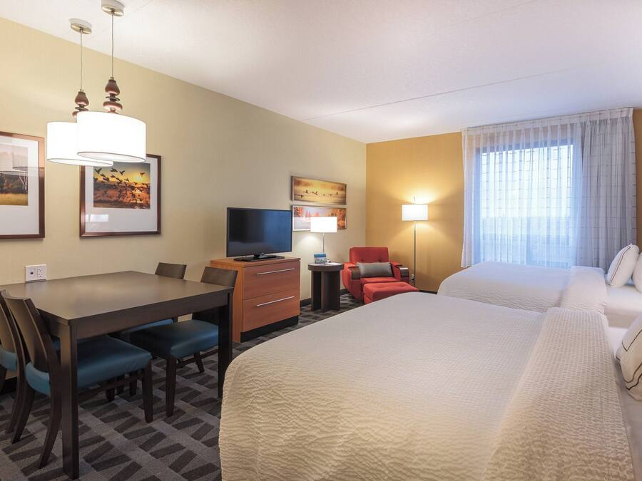 A hotel room with a large bed, a desk with a chair, a television, and a small table with a lamp.
