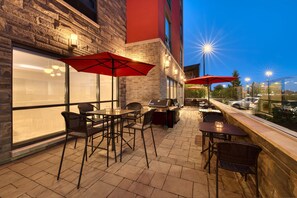 Een terras buiten met tafels, stoelen, een barbecue en parasols.