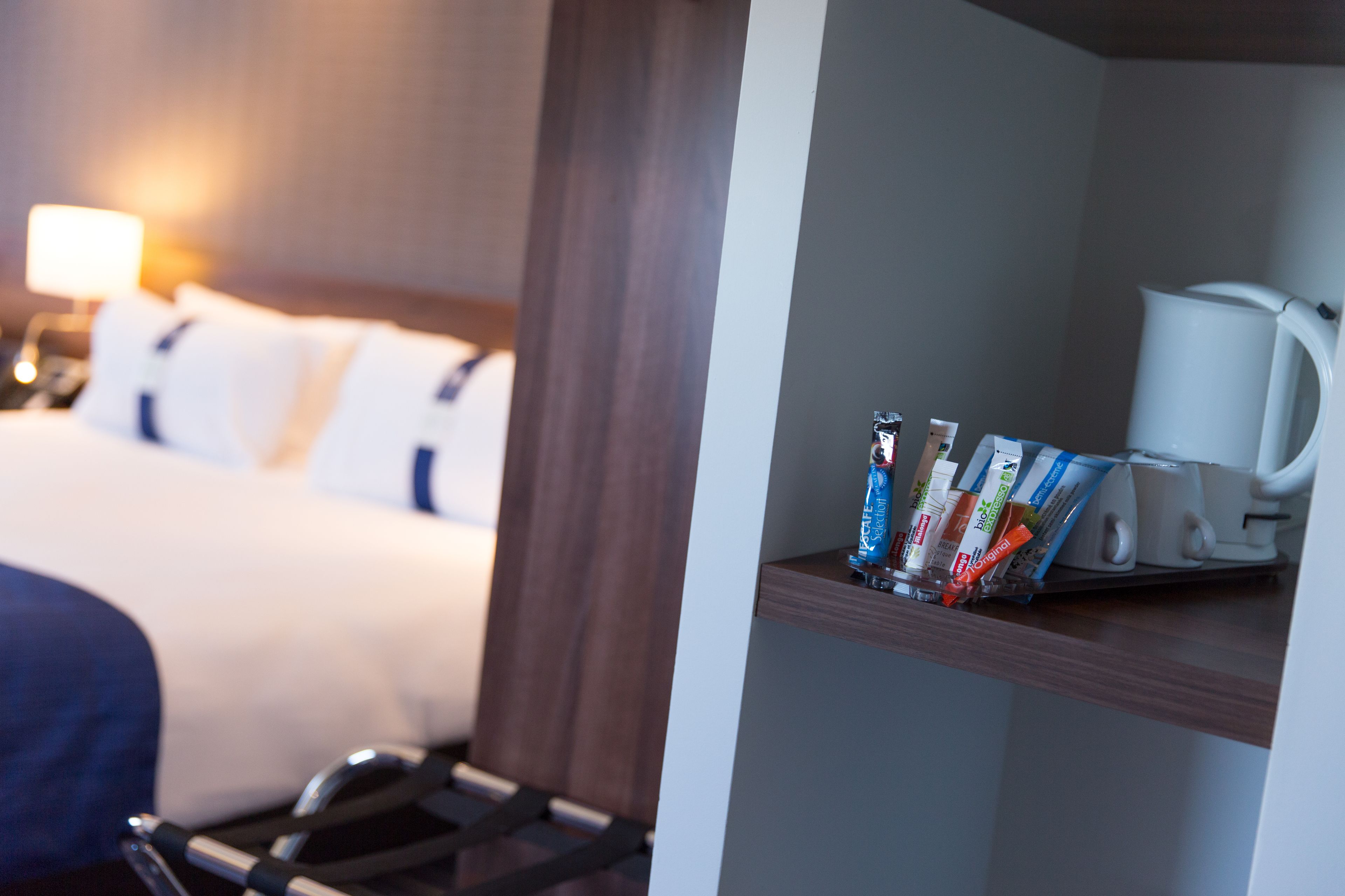 A hotel room with a neatly made bed, a bedside table with toiletries, and a coffee maker.