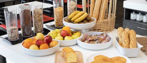 A buffet table with various food items including fruits, bread, and pastries.
