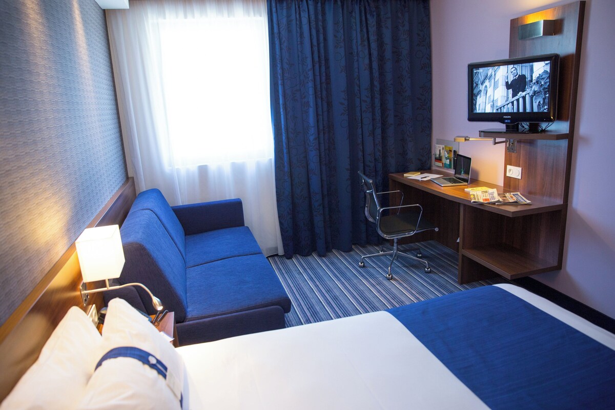 A hotel room with a bed, a desk, a chair, a television, and a window with curtains.
