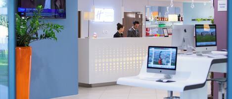A reception area with a TV displaying a movie, a desk with a computer, and a counter with a glass display.