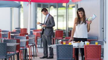 Un café en plein air avec des tables et des chaises, un homme qui lit un menu et une femme qui tient un menu.