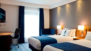 A hotel room with two beds, a desk, a chair, a television, and a large window with curtains.