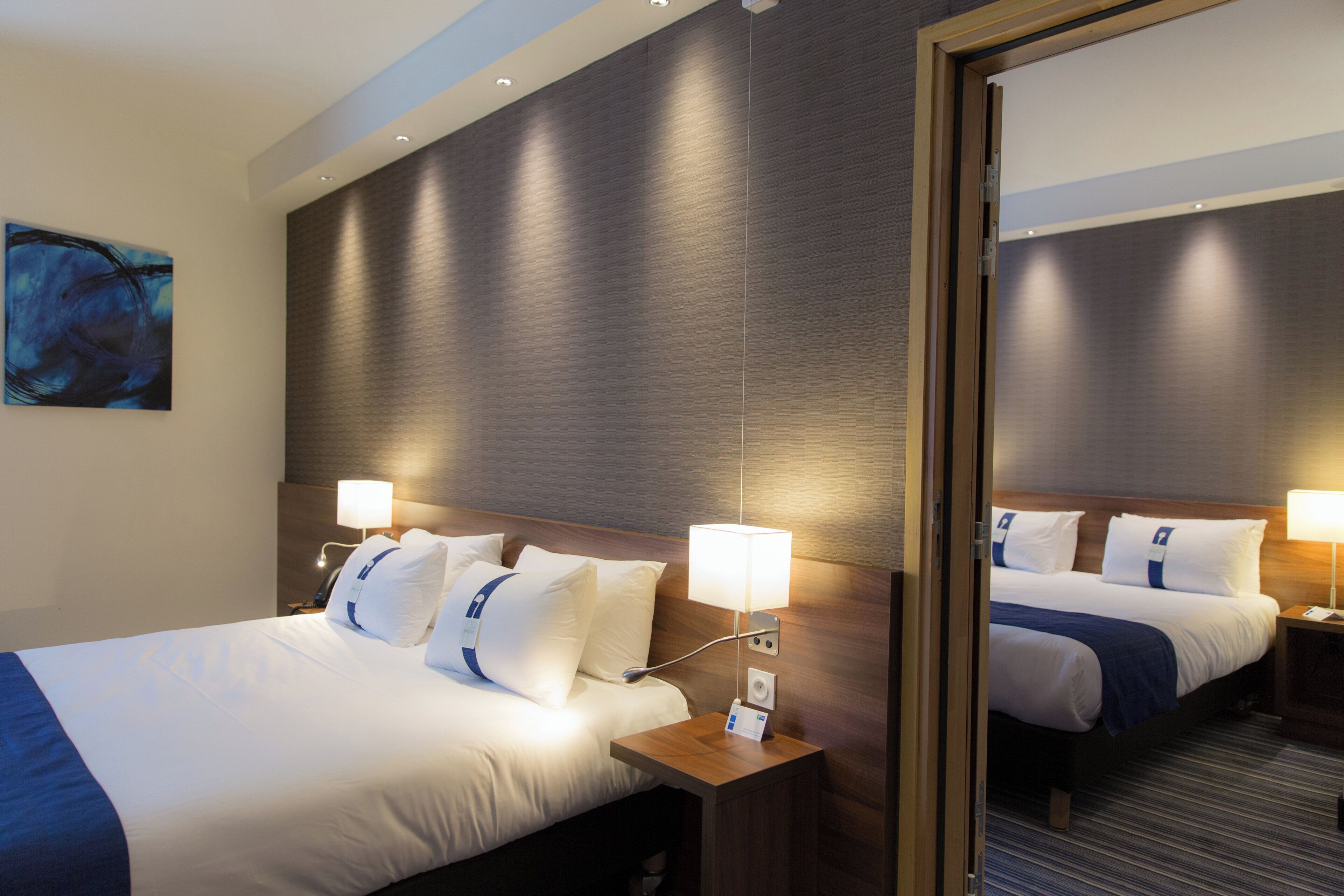 A hotel room with a large bed, bedside tables, a wall-mounted lamp, and a mirror.