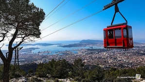 A red cable car suspended over a city with a clear view of the coastline and water.