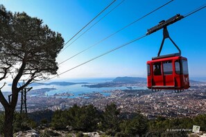 A red cable car suspended over a city with a clear view of the coastline and water. - Holiday Inn Express Toulon - Est by IHG (Toulon)