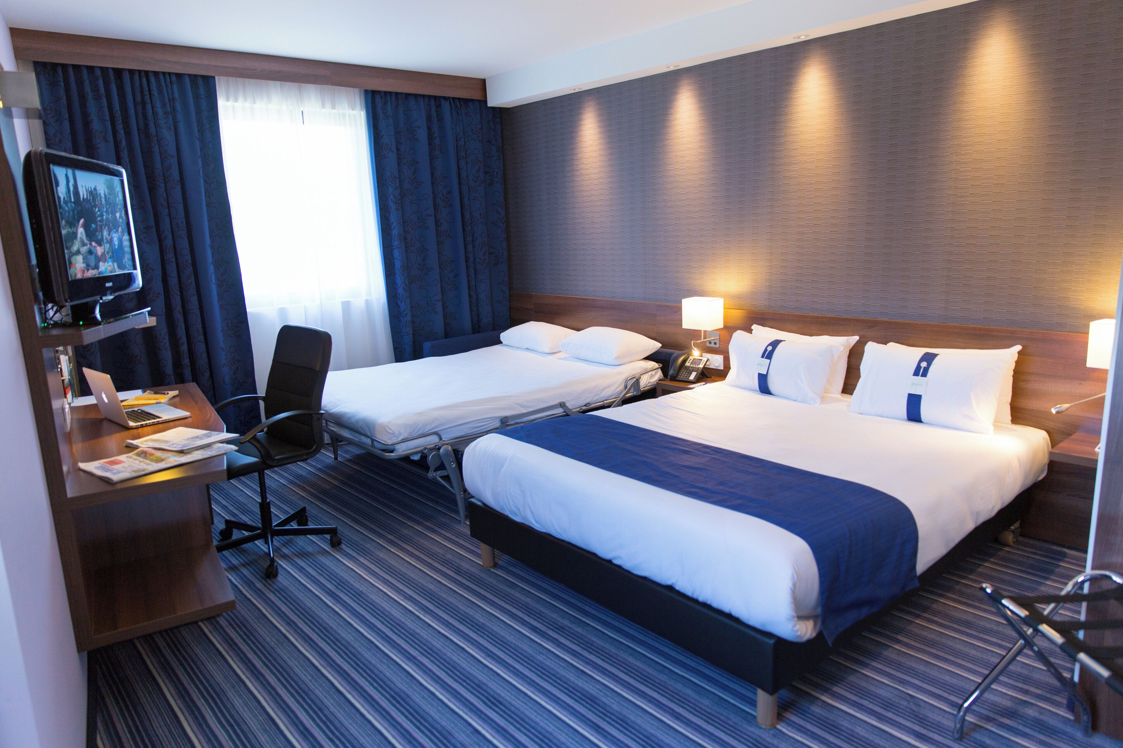 A hotel room with two beds, a desk with a laptop, a chair, and a TV.