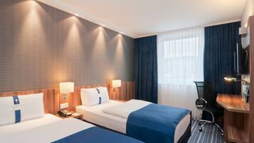 A hotel room with two beds, a desk, a chair, a TV, and a window with curtains.