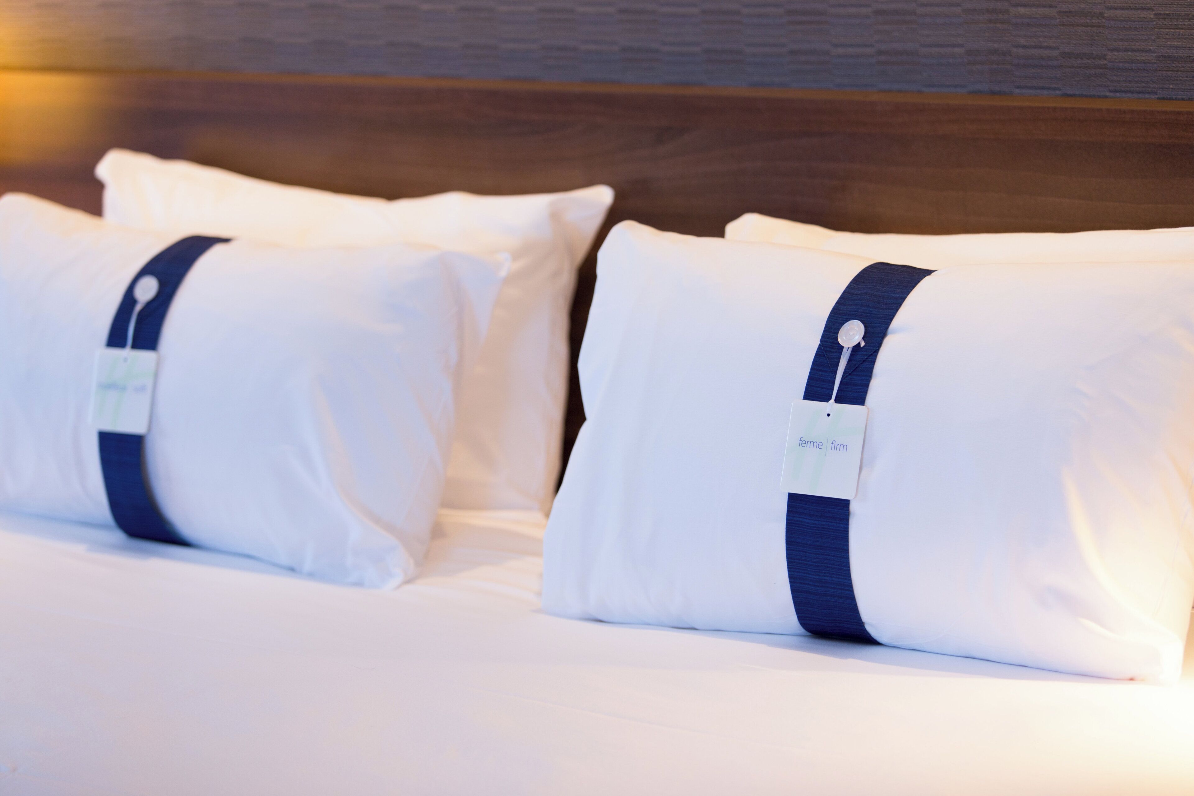 A neatly made bed with white bedding and pillows, each with a tag.