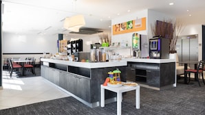 A modern kitchen with a central island, a dining area with red chairs, and a coffee machine.