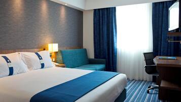 A hotel room with a bed, a desk, a chair, and a window with curtains.