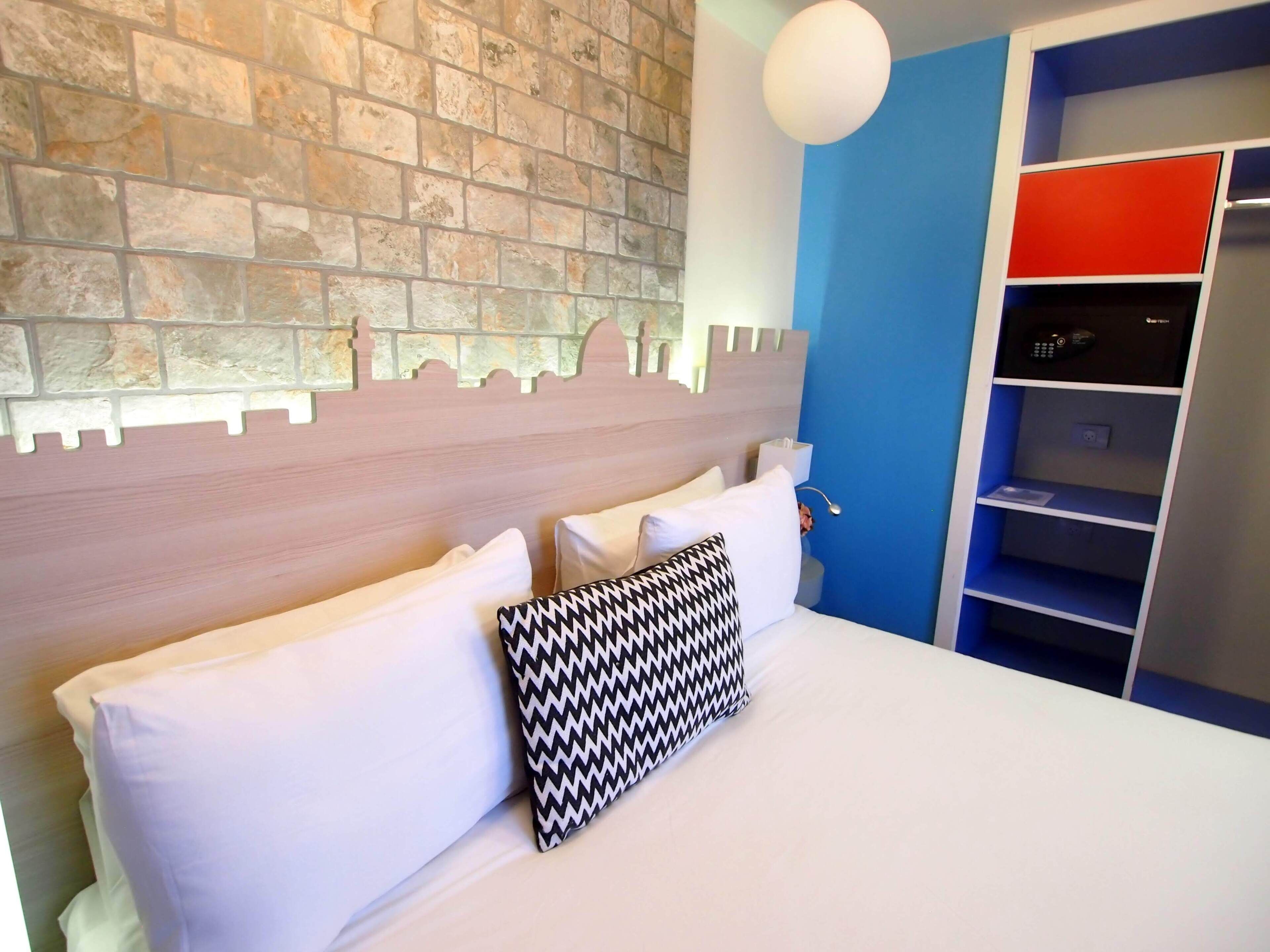 Ein Hotelzimmer mit einer Steinstur, einem Bett mit weiß und schwarzen Kissen und einer blauen Wand mit einem roten Regal.