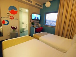 Habitación de hotel con dos camas, televisión, baño y vista a la ciudad.