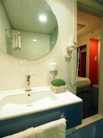 Un baño con un espejo grande, un lavamanos, un secador de manos y una pequeña planta en maceta.