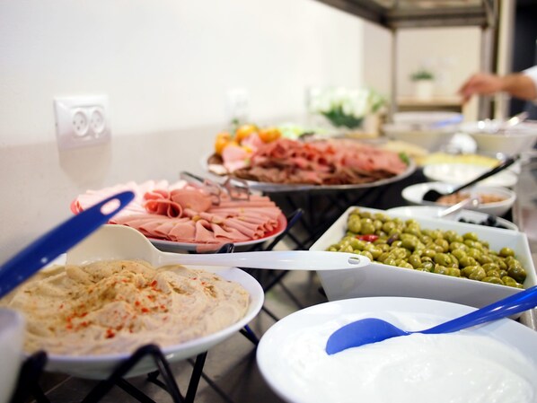 A buffet table with various food items including meats, dips, and olives.