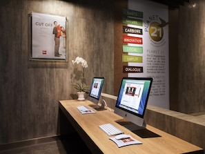 A reception desk with two monitors, a potted orchid, and a framed poster. - ibis Makassar City Center (Makassar)