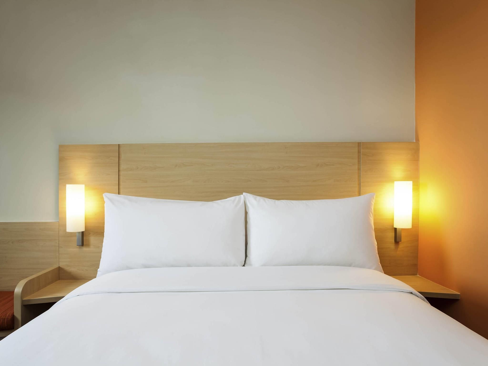 A hotel room with a wooden headboard, two bedside lamps, and a neatly made bed.