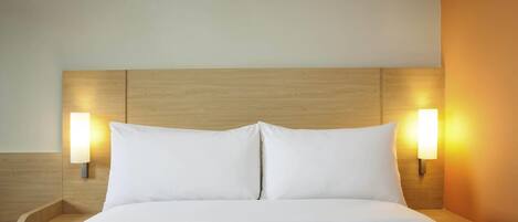 A hotel room with a wooden headboard, two bedside lamps, and a neatly made bed.