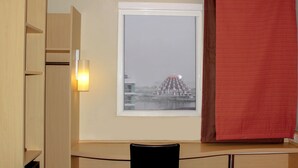 A room with a window overlooking a building, a desk with a chair, and a red curtain. - ibis Makassar City Center (Makassar)