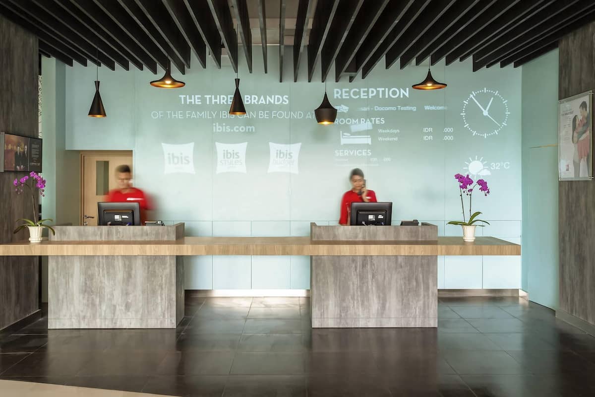 A reception desk with two staff members, a clock, and a digital display.