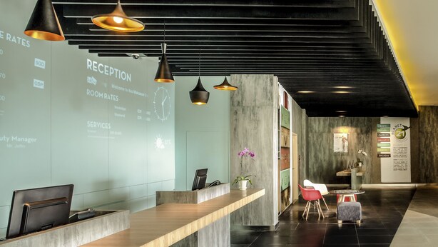 A reception area with a reception desk, a clock, and a wall displaying room rates and services. - ibis Makassar City Center (Makassar)