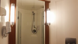 A bathroom with a glass-enclosed shower, a mirror with lights, and a wall-mounted hairdryer. - ibis Makassar City Center (Makassar)