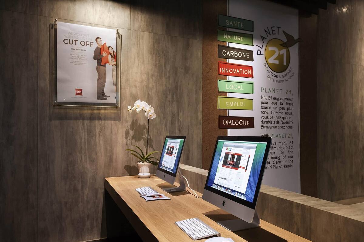 A reception desk with two Apple iMac computers, a potted orchid, and a framed poster.