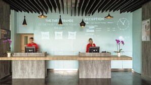 A reception desk with two staff members, a clock, and a temperature display. - ibis Makassar City Center (Makassar)