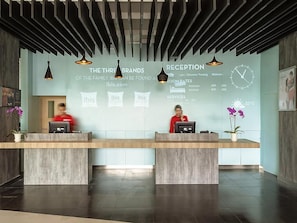 A reception desk with two staff members, a clock, and a temperature display. - ibis Makassar City Center (Makassar)