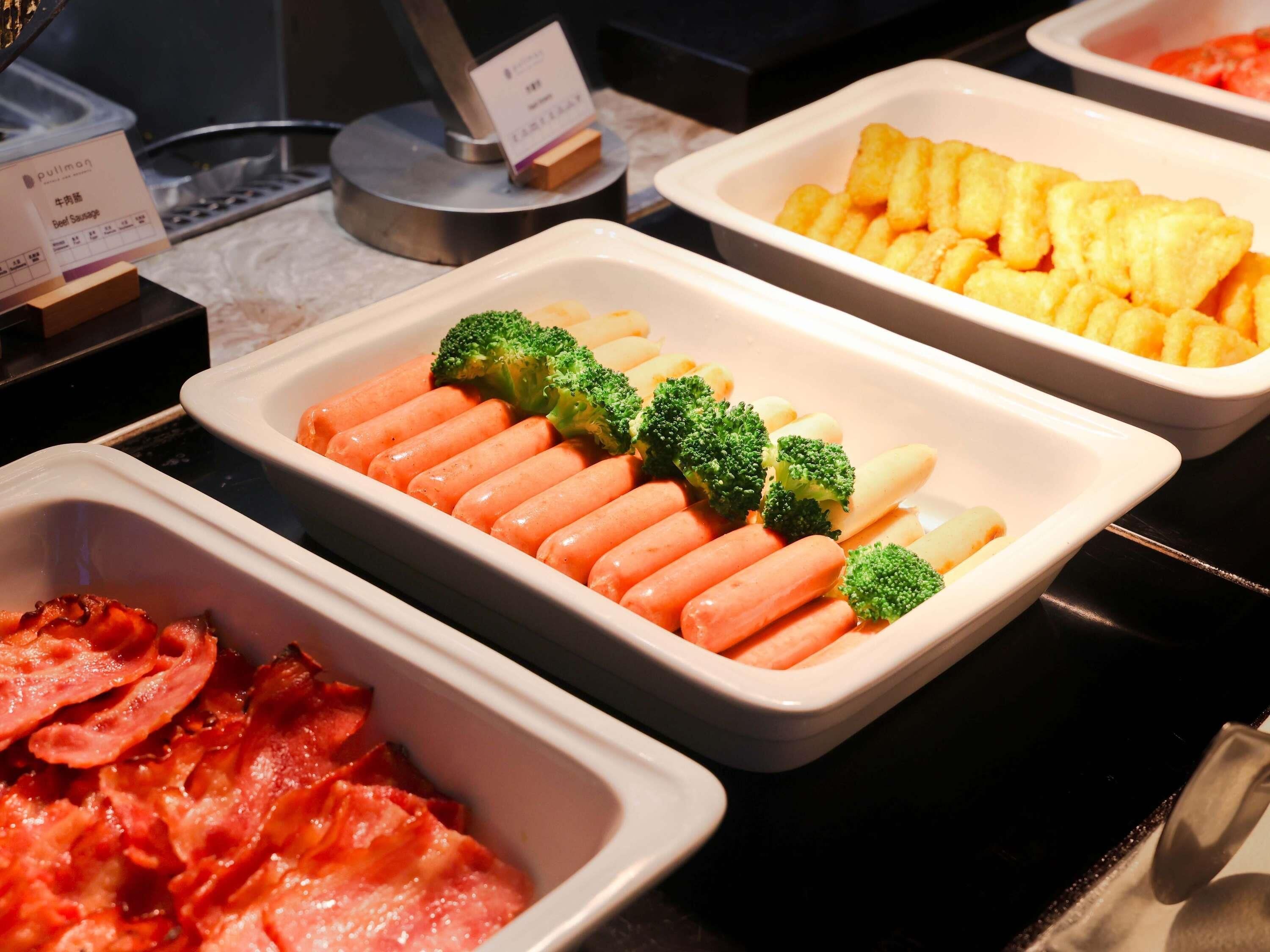 A buffet with various food items including sausages, broccoli, and potatoes.
