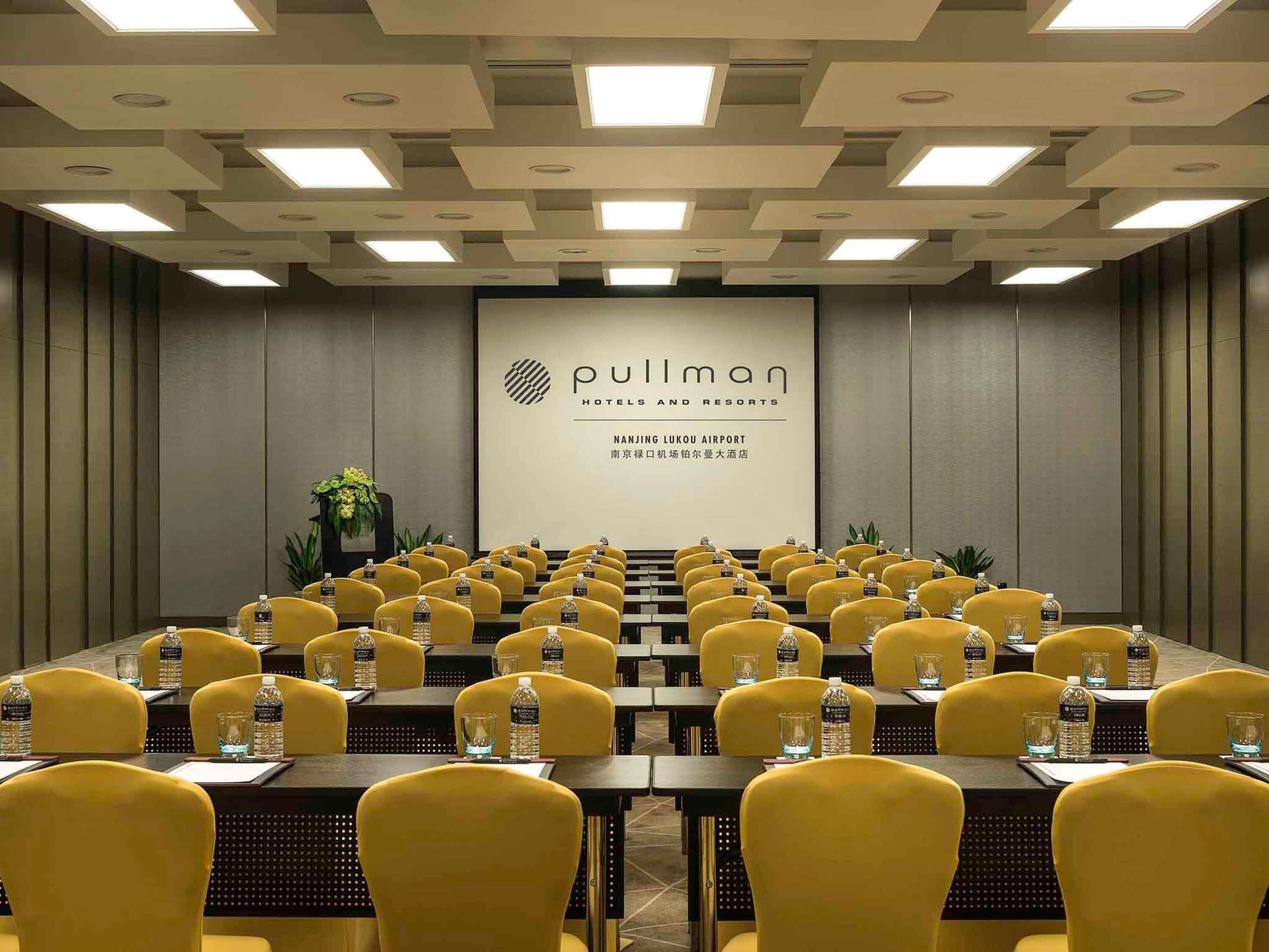 A conference room with yellow chairs, tables, and a large screen displaying 'Pullman Hotels and Resorts' branding.