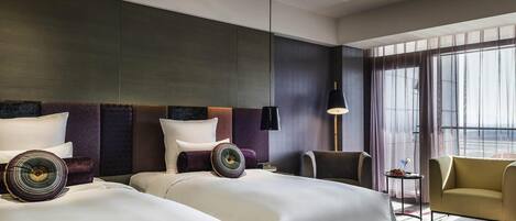 Ein Hotelzimmer mit zwei Betten, einer Sitzecke inklusive Sessel und Tisch sowie einem großen Fenster.